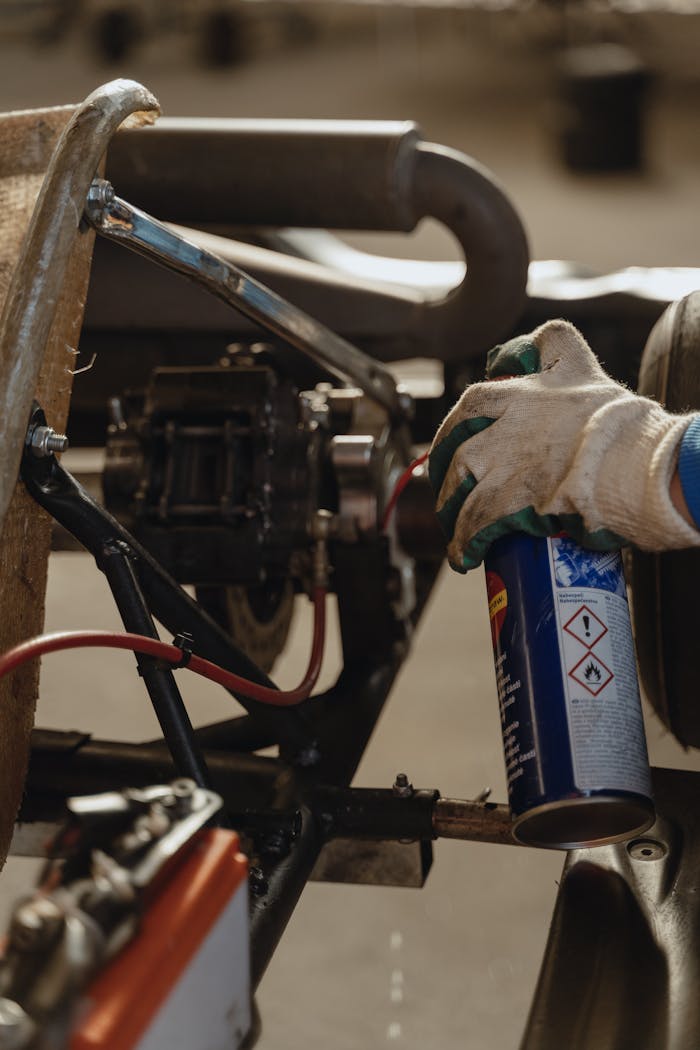Close-up of a mechanics glove holding lubricant spray while servicing a kart vehicle.