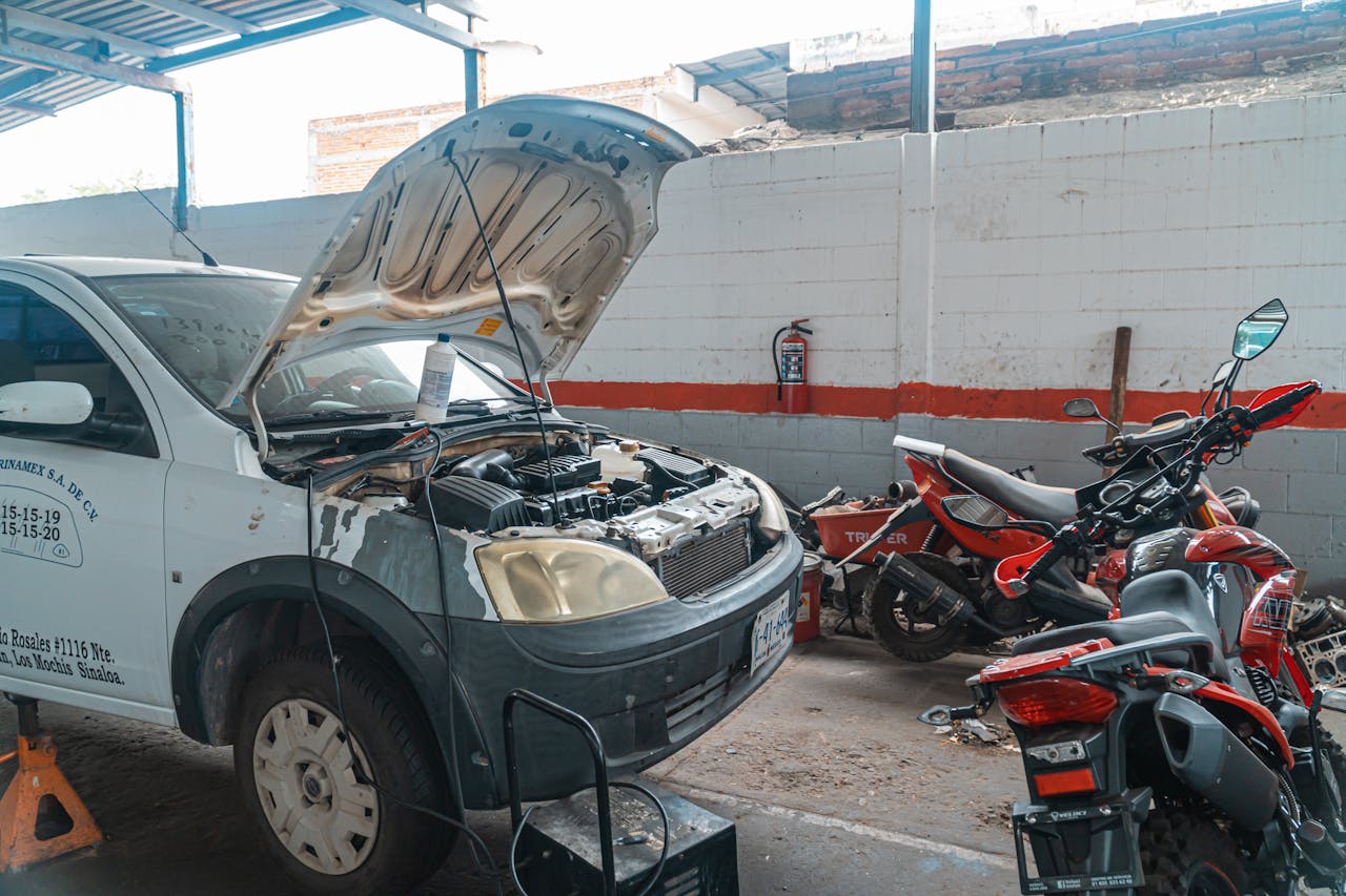 Car being repaired in a garage with motorcycles and tools around.